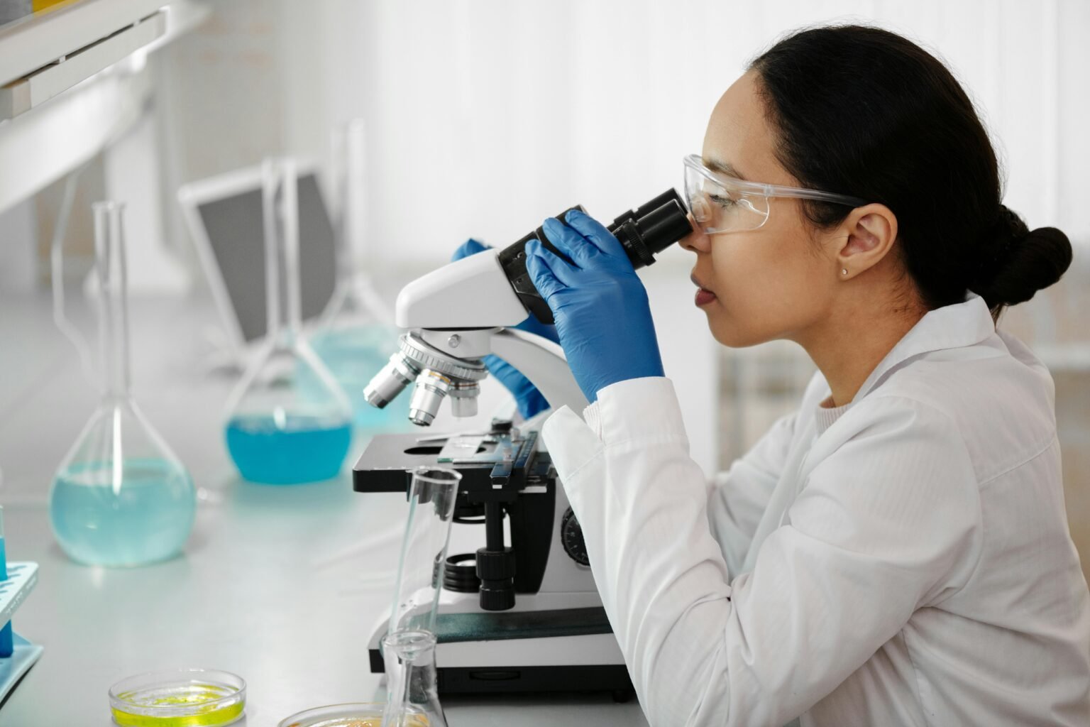 Female scientist in a laboratory examining samples through a microscope for research.